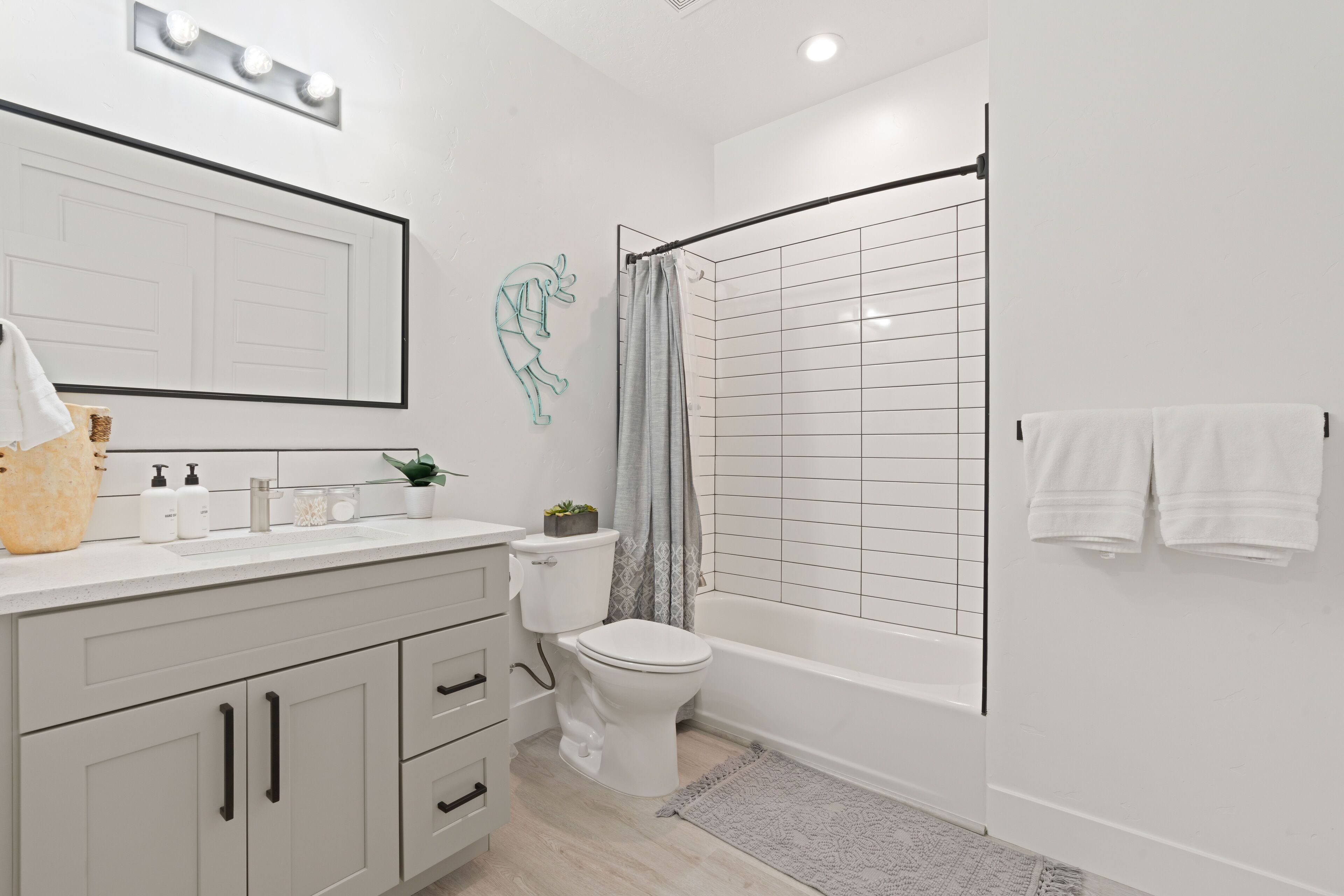Een moderne badkamer met een witte wastafel, toilet, bad en douchegordijn.
