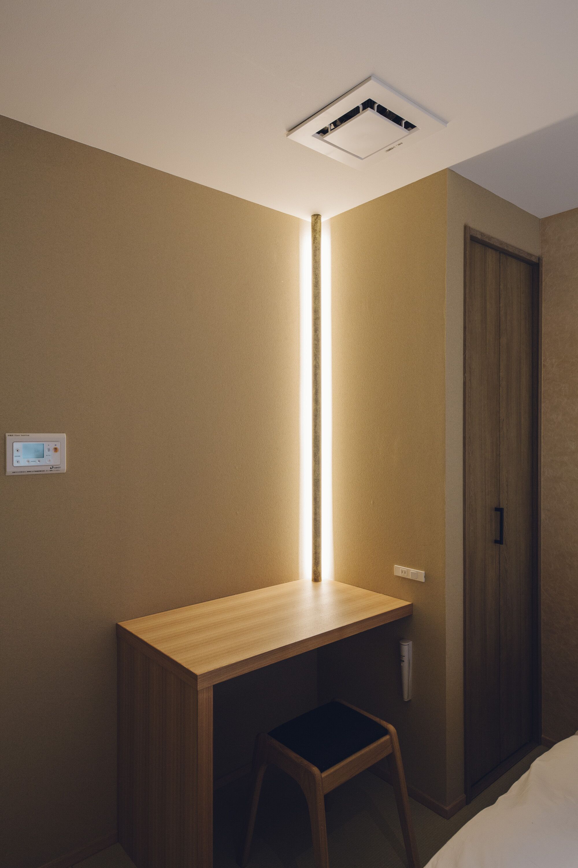 A room with a wooden desk, a chair, a wardrobe, and a ceiling light fixture.