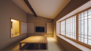 Una habitación japonesa tradicional con suelo de tatami, una mesa de madera baja, puertas correderas y un amplio ventanal con diseños de papel.