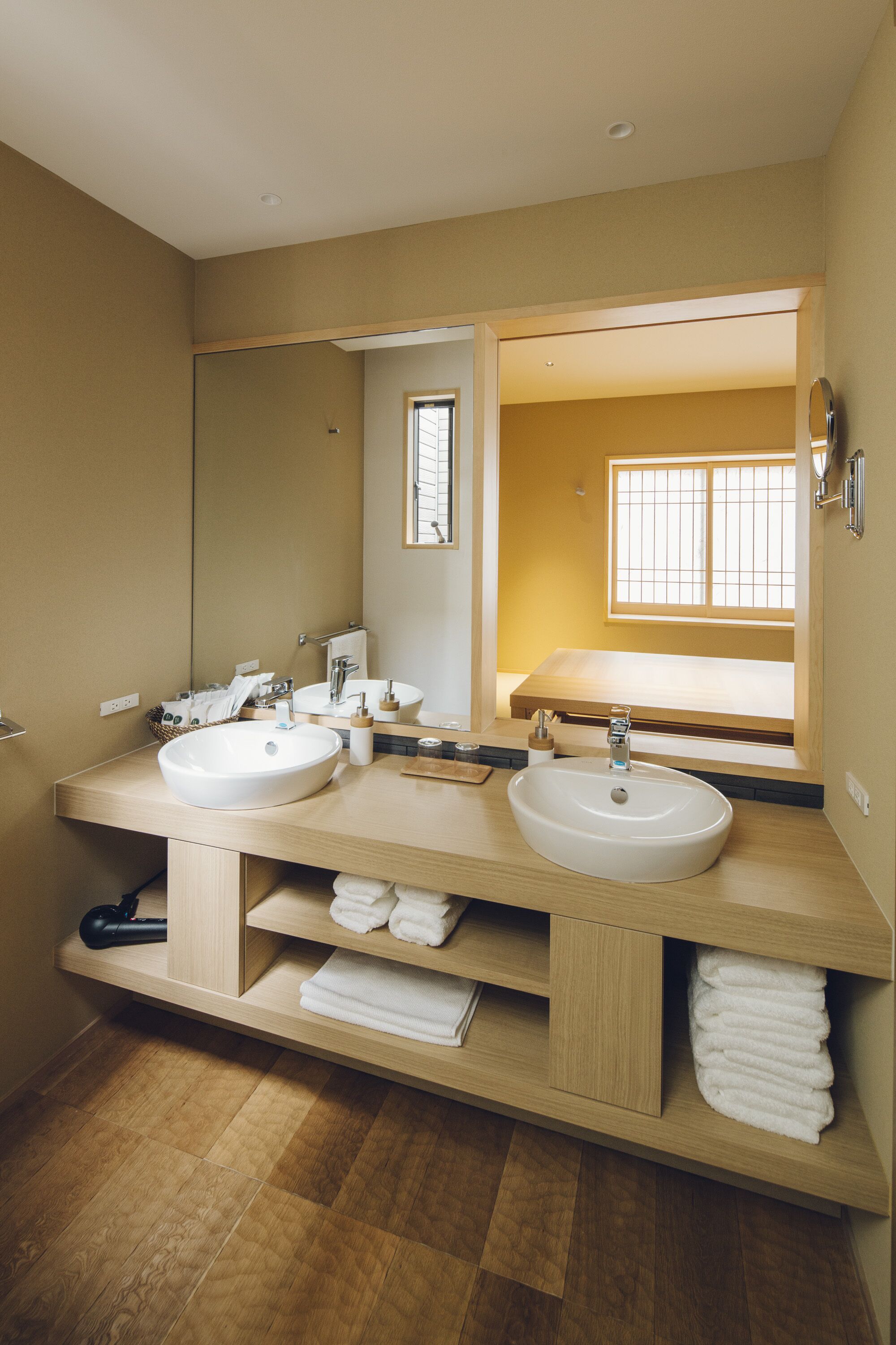 A modern bathroom with two sinks, a large mirror, and a window providing natural light.