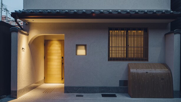 Una casa tradicional japonesa con una puerta de madera, una ventana pequeña con barrotes verticales y un buzón.