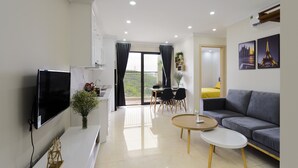 A modern living room with a flat-screen TV, a sofa, a dining table with chairs, and a balcony with curtains.