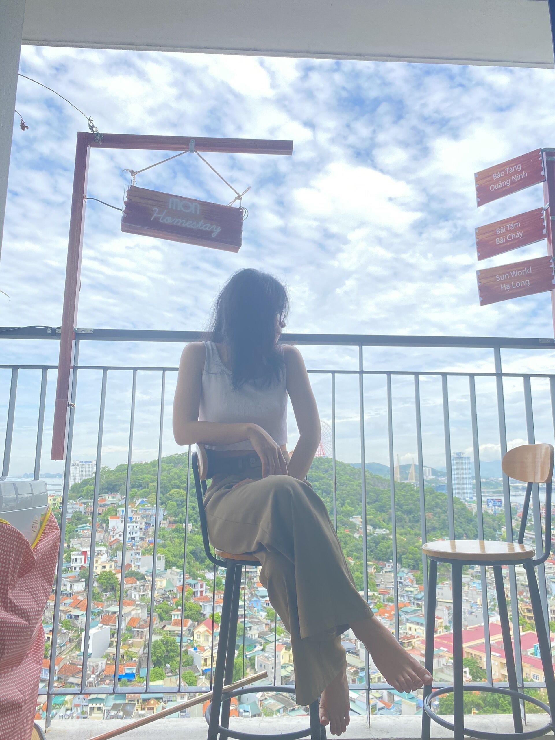 Eine Person sitzt auf einem Balkenstuhl mit Blick auf eine Stadtlandschaft und einem Schild mit der Aufschrift 'Home Holiday'.