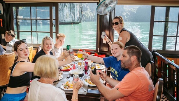 A group of people dining at a table with a view of a body of water and cliffs.