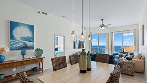 Een ruime woonkamer met een grote eettafel, zithoek en uitzicht op de oceaan door grote ramen.