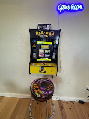 Una máquina de videojuegos de Pac-Man con un letrero de neón encima y una mesa de pinball de Turtles in Time debajo.