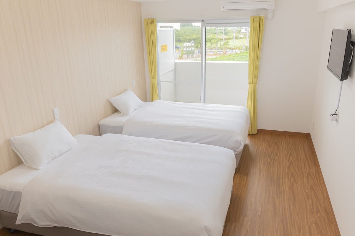 A hotel room with two beds, a TV, and a view of greenery outside.