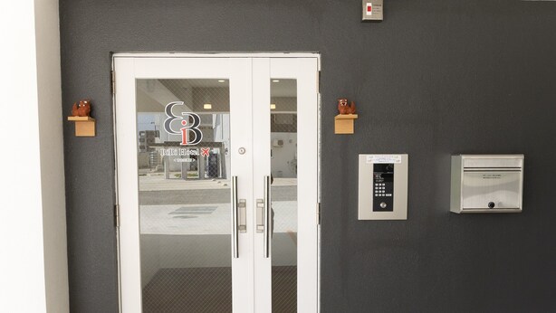 A hotel entrance with a glass door, a keypad entry system, and two small wall-mounted lights. - BIBI HOTEL MIYAKO KUKOMAE (Miyakojima)