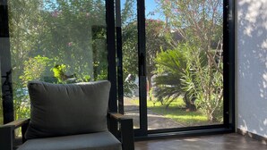 A room with a grey sofa, a large sliding glass door, and a view of a garden with various plants and trees. - 3 Bedroom Apartment with pool (Celuga)