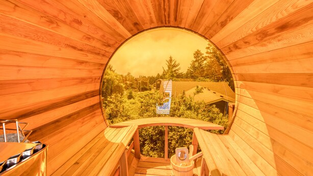Un interior de madera con un ventanal circular que ofrece vistas a un área boscosa y un edificio.