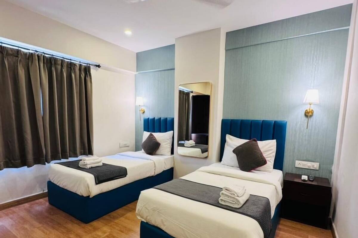 A hotel room with two beds, a ceiling fan, a large mirror, and a nightstand with a lamp.