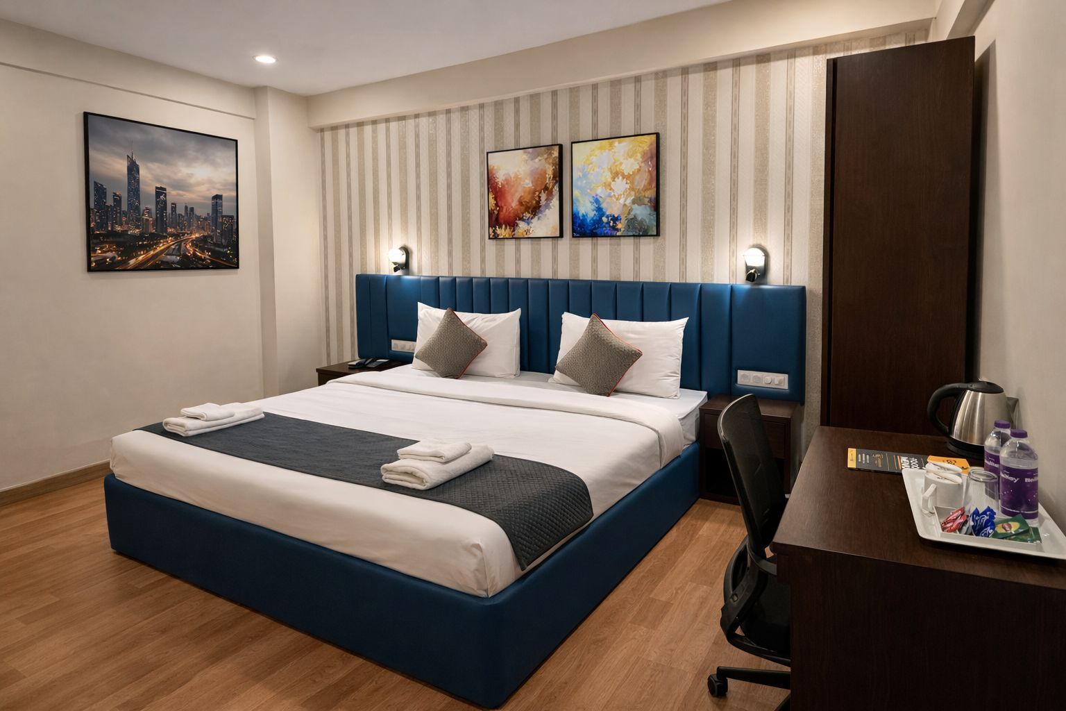 A hotel room with a large bed, a desk, a chair, and artwork on the walls.
