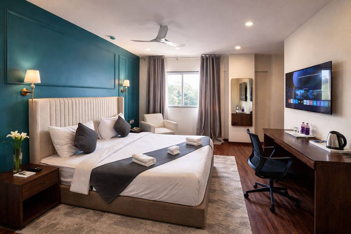 A hotel room with a bed, desk, chair, TV, and a view of the outdoors.