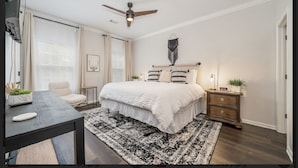 Une chambre à coucher comprenant un lit, des tables de chevet, un bureau et un ventilateur de plafond.