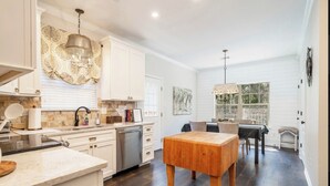 Une cuisine spacieuse avec des meubles blancs, une table à manger en bois et une vue sur l’extérieur grâce à de grandes fenêtres.