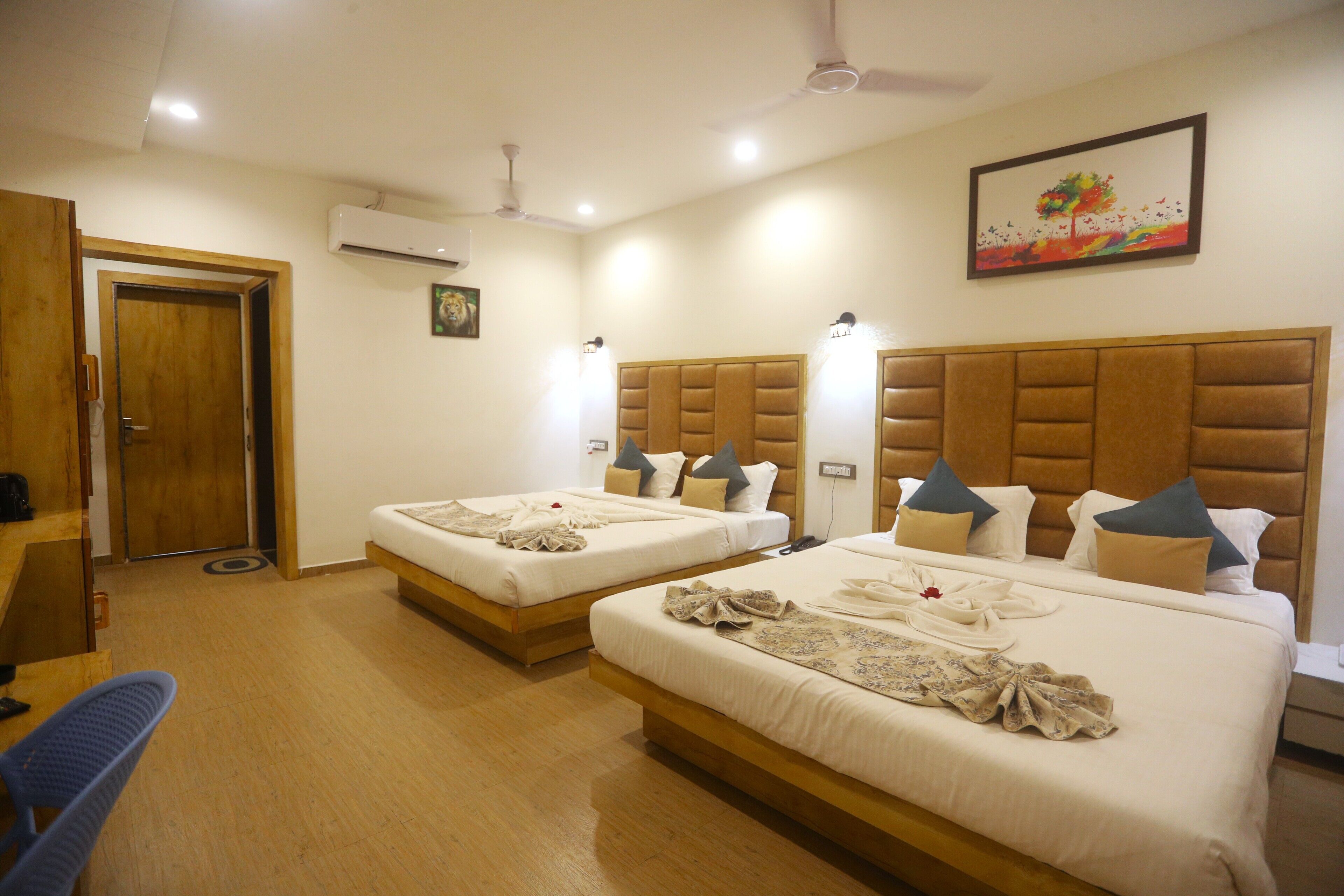 A hotel room with two beds, a wooden floor, an air conditioning unit, a ceiling fan, and a painting on the wall.