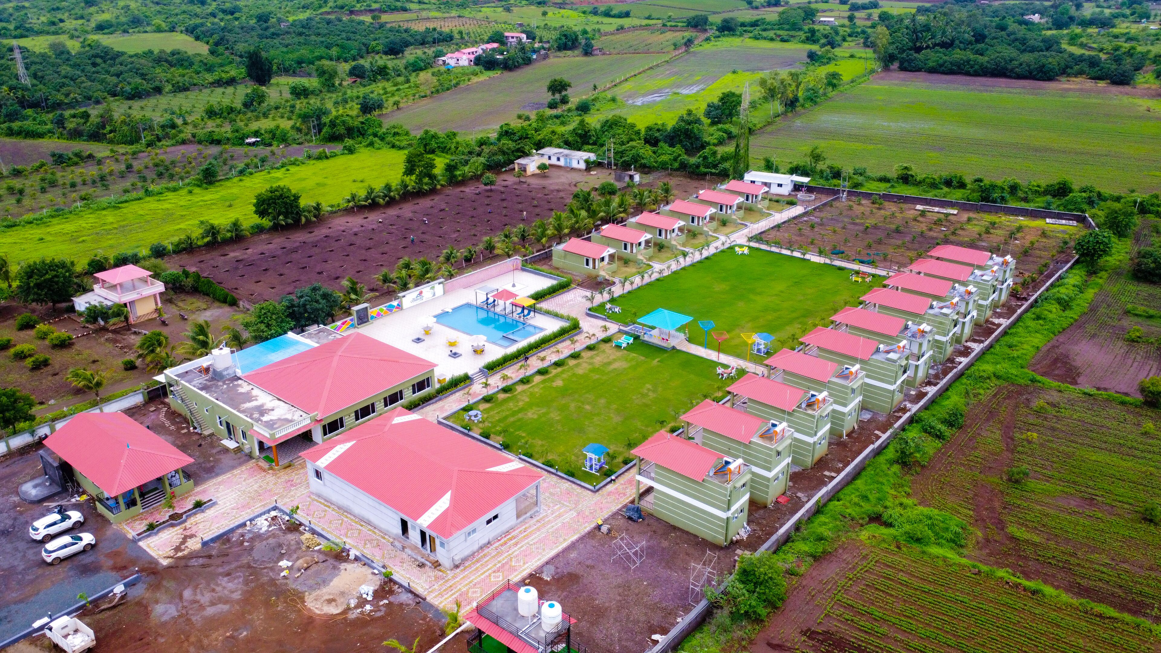 An aerial view of a residential area with multiple houses, a swimming pool, and green fields.