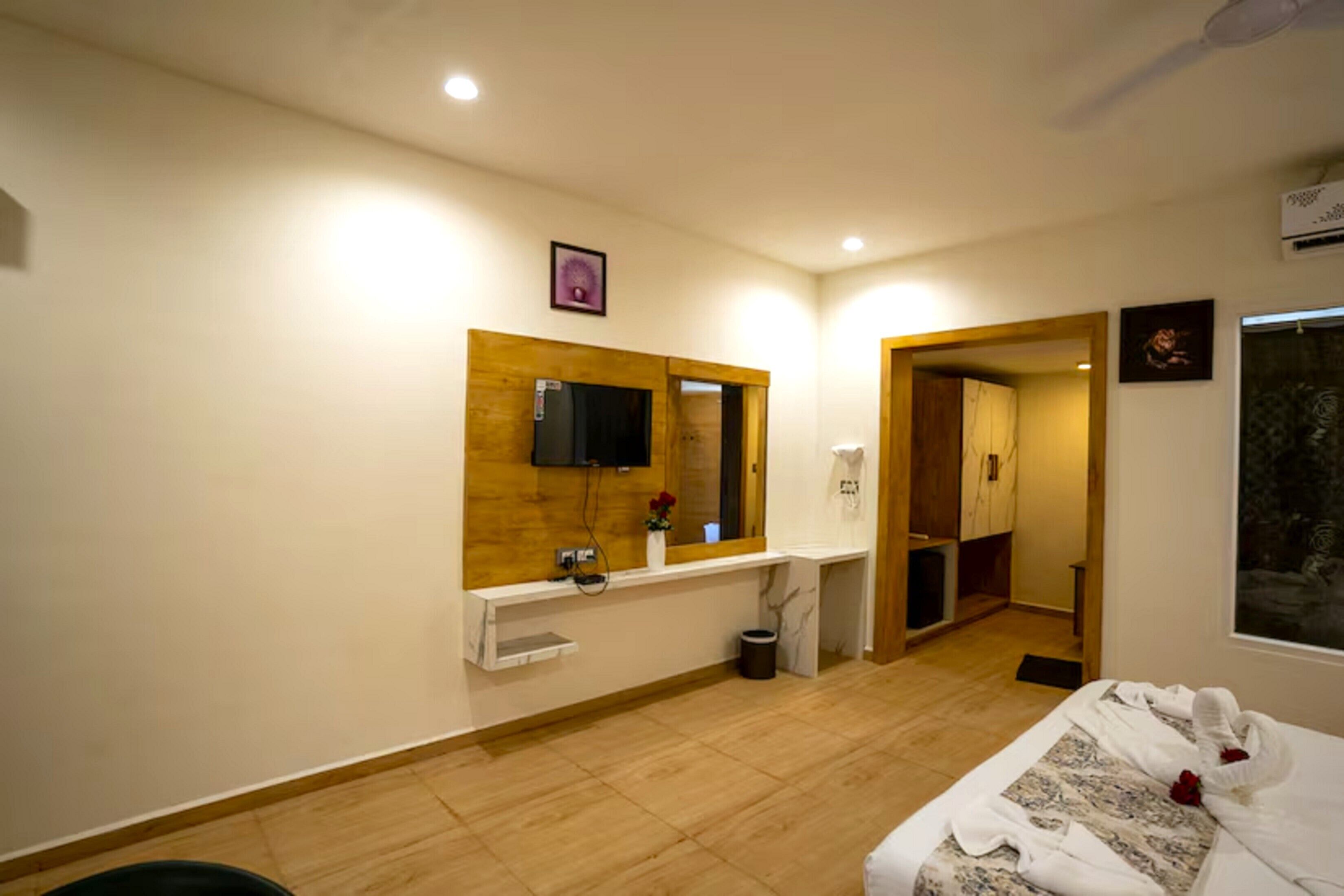 Ein Hotelzimmer mit einem Holznähtischchen, einem Flachbildfernseher, einer kleinen Ablage mit einer Vase und einem Bett mit ordentlich gefalteten Handtüchern.