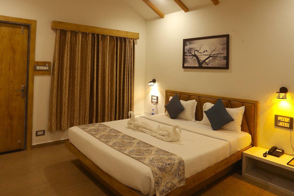 Un dormitorio con techo de madera, una cama con almohadas, una mesita de noche con una lámpara y un cuadro en la pared.