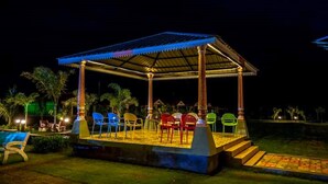 A gazebo with a metal roof and columns, surrounded by chairs and a small stage. - The Comfort Gir Resort (Mendarda)