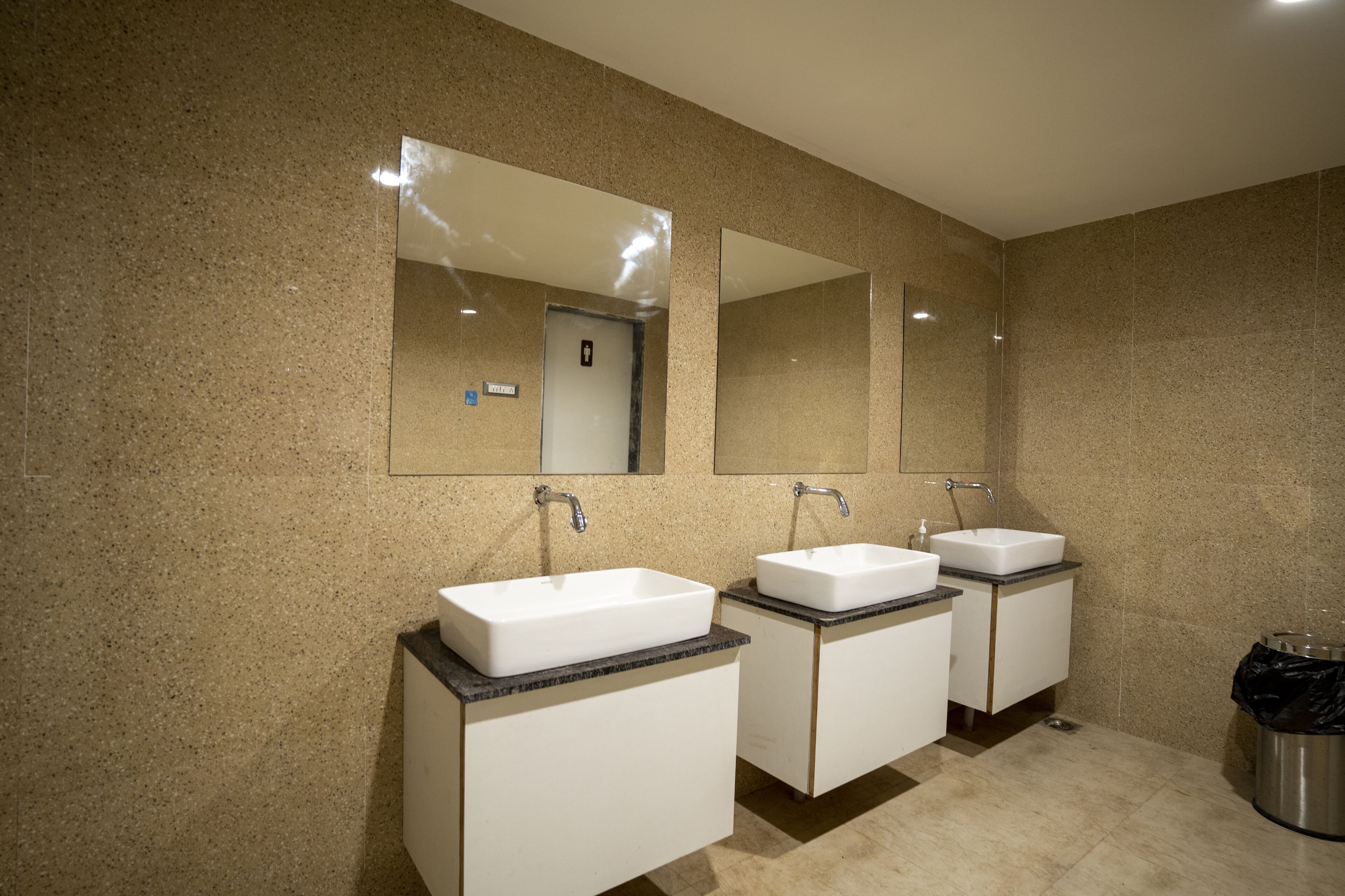 A modern bathroom with two sinks, large mirrors, and a trash can.