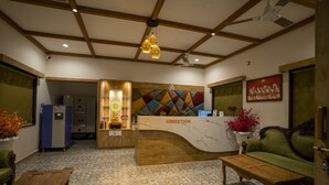 A reception area with a marble counter, wooden ceiling beams, patterned floor tiles, a green sofa, and a wooden coffee table. - The Comfort Gir Resort (Mendarda)