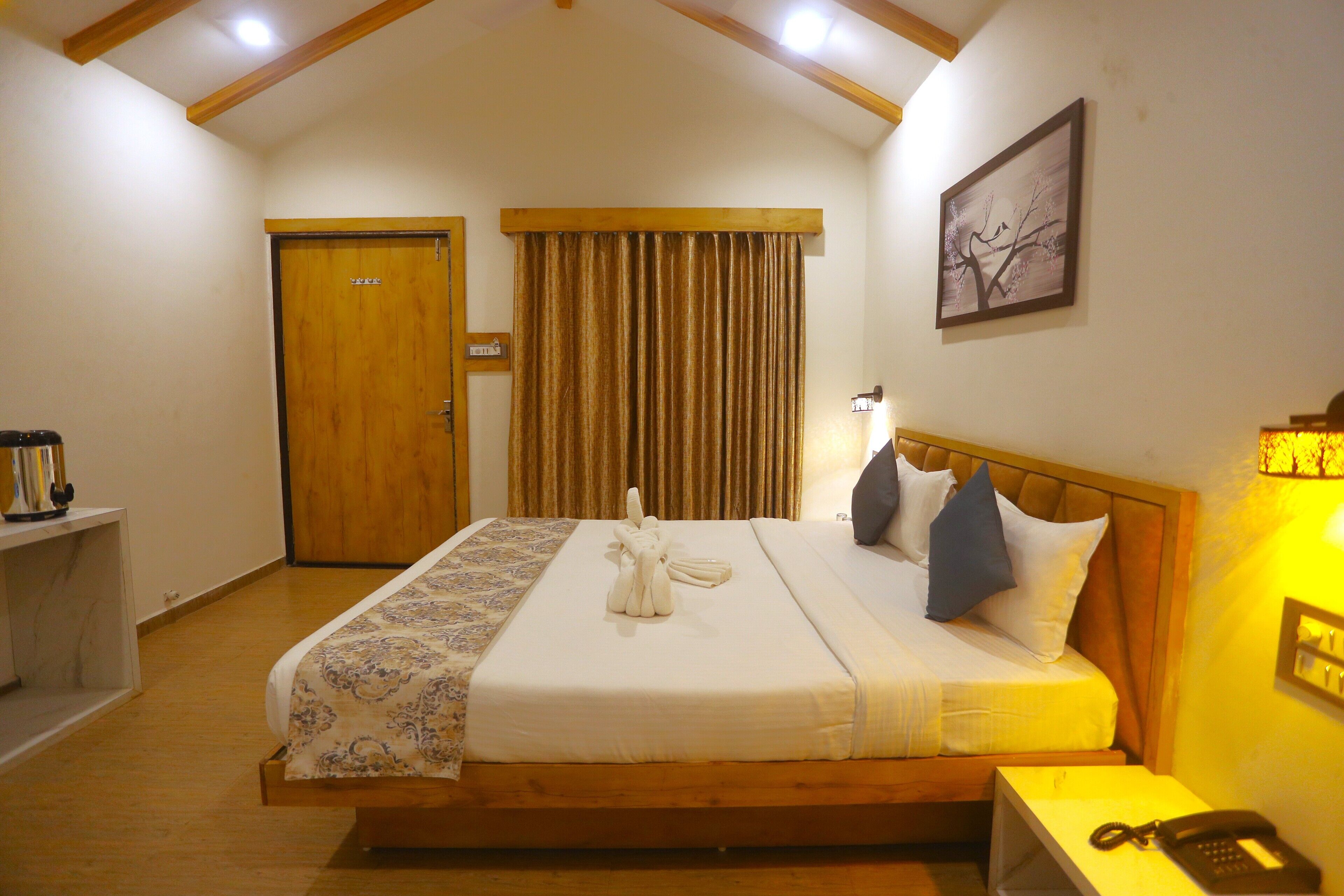 Una habitación de hotel con una cama de madera, una mesita de noche con una lámpara, una puerta y un cuadro enmarcado en la pared.