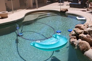 A swimming pool with a blue floating device, clear water, and surrounding rocks. - UN Non-Profit Rates: Exceptional Value Near Mayo, Kirkland, WestWorld etc. (Scottsdale)
