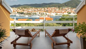 Un balcón con dos sillones de madera, una planta en maceta y vistas a un pueblo y montañas.