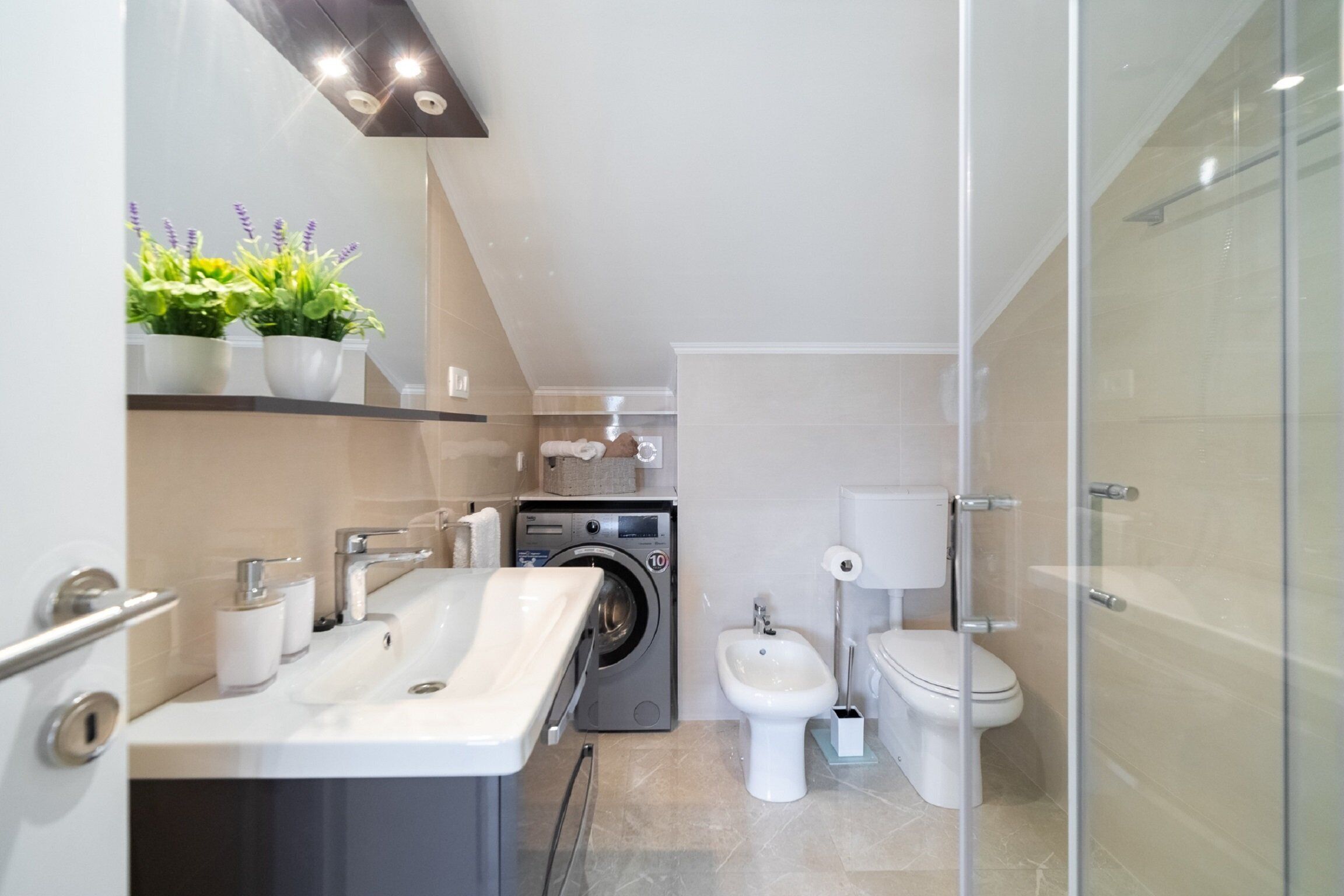 Un baño moderno con lavamanos, espejo, lavadora, inodoro y ducha.