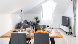 Un área de comedor moderna con una mesa de madera dispuesta para una comida, un sofá y un televisor al fondo.
