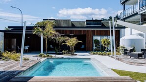 Ein modernes Gebäude mit Pool, Holzterrasse und Sitzgelegenheiten im Freien.