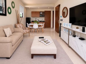 A modern living room with a sofa, a dining table with chairs, a kitchen area, and a TV.