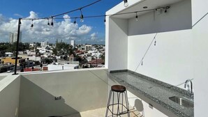 A balcony with a view of a cityscape, a bar area with a sink, and string lights. - Rooftop Pool Apt for 4 | Near Isla Ferry, Cancun (CancÃºn)