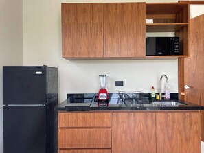 A kitchen with wooden cabinets, a black refrigerator, a red blender, and a microwave. - Rooftop Pool Apt for 4 | Near Isla Ferry, Cancun (CancÃºn)