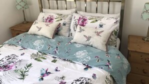 Un lit avec une literie à motifs floraux et d’oiseaux, une tête de lit en bois et deux tables de chevet avec des lampes.