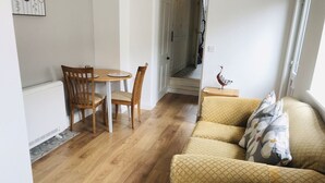 Un salon doté d’un plancher en bois, d’un canapé jaune, d’une table à manger avec des chaises et d’une petite table d’appoint sur laquelle est posé un objet décoratif.