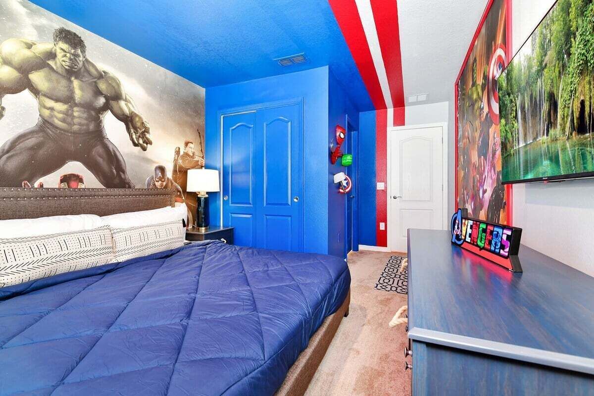 Un dormitorio con una cama grande, una puerta azul, un televisor y un mural en la pared.