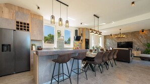 Una cucina moderna con isola centrale, sgabelli da bar e zona pranzo con divano e televisore.