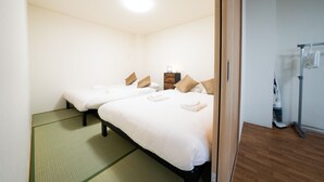 A hotel room with two beds, a wooden floor, a visible vacuum cleaner, and a mirror reflecting part of the room. - Sakimoto Residence Namba Minami III (Osaka)
