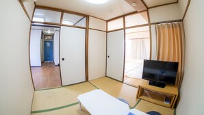A room with tatami flooring, a bed, a television on a wooden stand, and a sliding door leading to another room. - Sakimoto Residence Namba Minami III (Osaka)