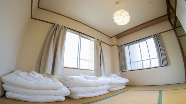A room with tatami mats, a stack of white towels, and two windows with curtains. - Sakimoto Residence Namba Minami III (Osaka)