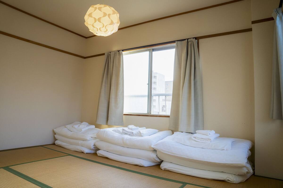 A hotel room with tatami mats, a large window with curtains, and neatly folded towels on the floor.