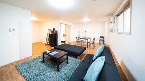A modern living room with a black sofa, a coffee table, and a dining area with chairs and a table. - Sakimoto Residence Namba Minami III (Osaka)