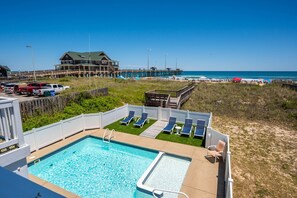 A pool area with lounge chairs, a wooden deck, and a view of the beach and pier.