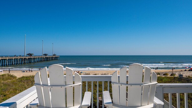 A beach view with white chairs and a pier in the background.