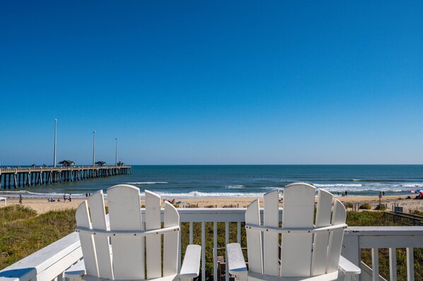 A beach view with white chairs and a pier in the background.