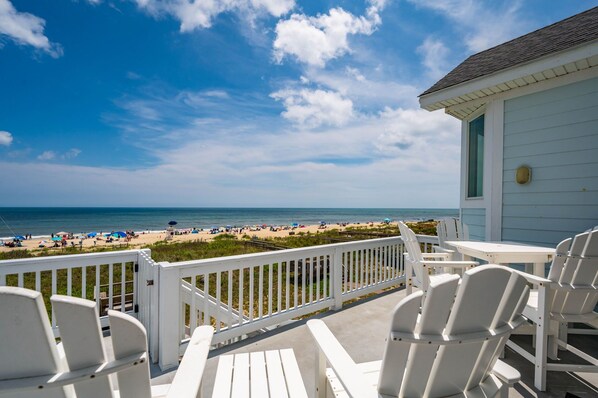A balcony with white chairs and a view of a beach with umbrellas.