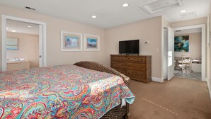 A bedroom with a large bed, a dresser, a television, and artwork on the walls.