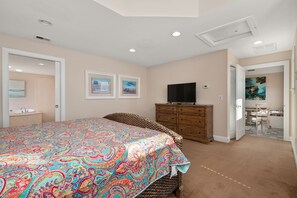 A bedroom with a large bed, a dresser, a television, and artwork on the walls.